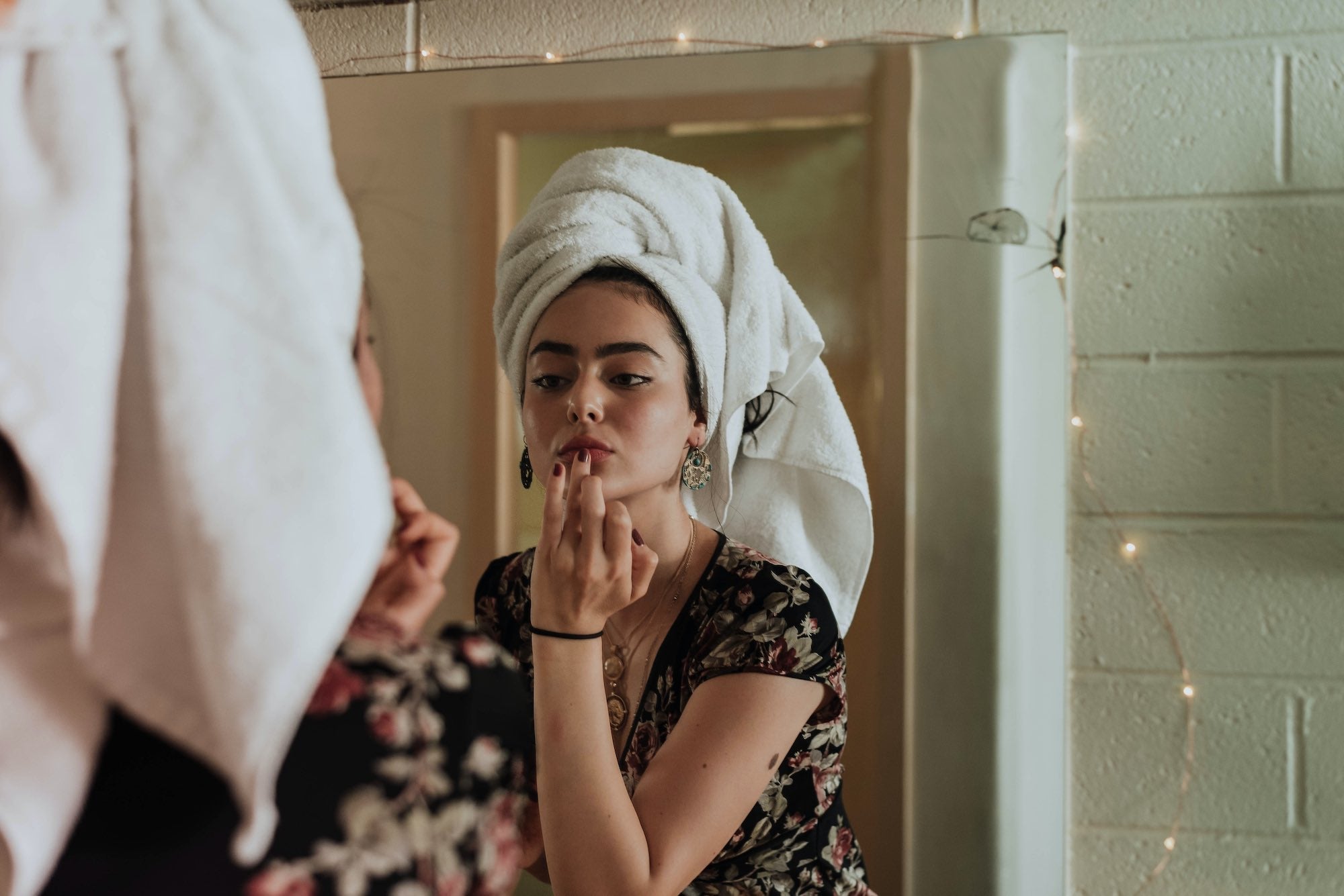 woman putting gloss or lipstick on looking in the mirror with a towel wrapped on her head